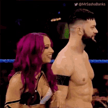 a man and a woman are standing next to each other in a wrestling ring . the woman has purple hair .