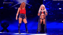 two women are standing next to each other on a blue stage .