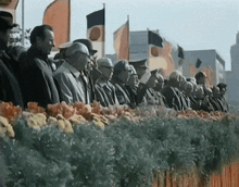 a group of people standing in front of a row of flowers and flags