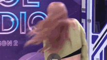 a woman with long red hair is standing in front of a purple sign that says ' a ' on it .