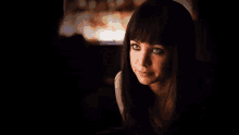 a woman with black hair and blue eyes looks at the camera in a dark room