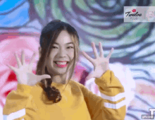 a girl wearing a yellow sweater is smiling and waving her hands