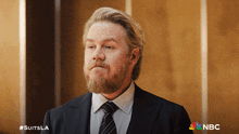a man with a beard is wearing a suit and tie with a nbc logo in the corner