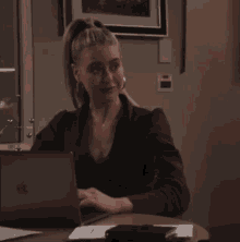 a woman sits at a desk with a laptop and a phone