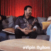 a man with a mustache is sitting on a couch next to a table with the words @vipin ayilam on it