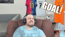 a man wearing headphones sitting on a couch with a sign that says goal behind him