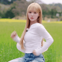 a woman in a white shirt and blue jeans is sitting in a grassy field