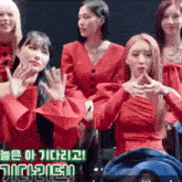 a group of women in red dresses are sitting next to each other and waving at the camera .