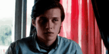 a young man is sitting in front of a red curtain in a room .