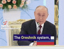 a man in a suit and tie speaking into a microphone with a sign that says the oreshnik system