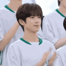 a young boy in a white shirt with a green collar is clapping his hands in a group of people .