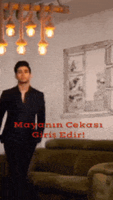 a man in a suit is standing in front of a green couch and a window with the words mayanin cekasi girişidir