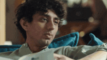 a man with curly hair is laying on a blue couch looking at a tablet