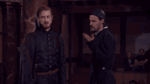 a man with a bandana on his head talks to another man in a dark room