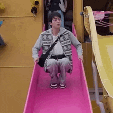 a young man is sitting on top of a pink slide .