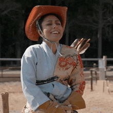 a woman wearing a cowboy hat and a kimono smiles with her eyes closed
