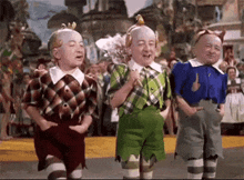 three dwarfs from the wizard of oz are standing next to each other on a street .