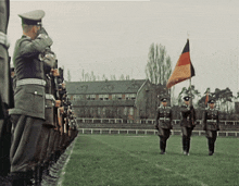 a group of soldiers marching in a field with a flag in the background