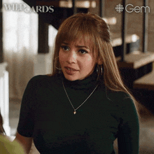 a woman wearing a green turtleneck necklace and hoop earrings is standing in front of a sign that says wild cards