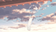 a wind chime is hanging from the roof of a building with a cloudy sky in the background .