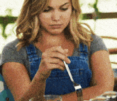 a woman in overalls is holding a silver fork