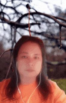 a woman wearing headphones looks at the camera with a tree branch hanging from her head