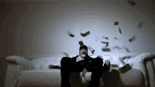 a man is sitting on a white couch with money falling from the ceiling