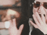 a close up of a person wearing sunglasses and covering their mouth