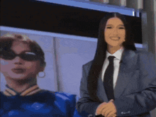 a woman in a suit and tie is standing in front of a picture of another woman