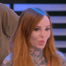 a woman with long red hair and a tattoo on her neck looks at the camera