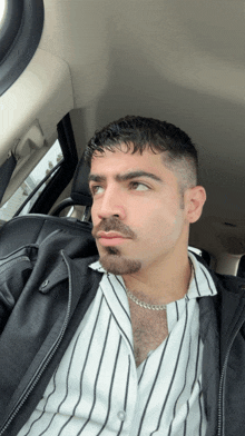a man in a striped shirt and a black jacket is sitting in the back seat of a car