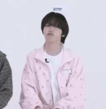 a young man wearing a pink jacket is sitting in front of a white wall .