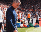 a man in a blue shirt walks on a soccer field with a blue cooler that says ' ambulance ' on it