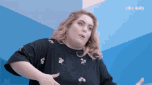 a woman in a black shirt is standing in front of a blue wall with the elite daily logo on it