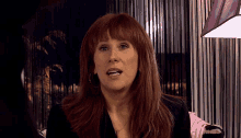 a woman with red hair is sitting in front of a purple curtain