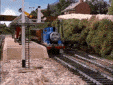a thomas the tank engine train is going down the tracks at a station .