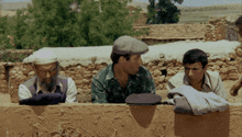 a man with a beard sits next to two other men on a wall
