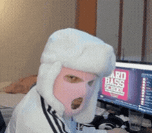 a man wearing a ski mask and a hat is sitting in front of a computer screen that says ard bass school