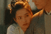 a man and a woman are standing next to each other . the woman is wearing a crown of flowers in her hair .