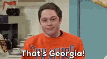 a man in a red sweatshirt is sitting in a kitchen and says `` that 's georgia ! ''