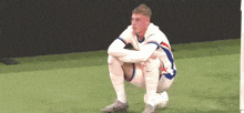 a soccer player is squatting on the field with his legs crossed and looking at the camera .