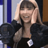 a woman is smiling in front of a microphone and covering her ears with her hands .