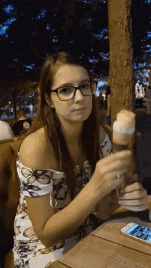 a woman sitting at a table holding a glass of beer and a ice cream cone