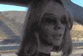 a woman wearing sunglasses is sitting in a car with mountains in the background