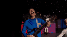 a man in a blue shirt is dancing in front of a drum that says wiggles