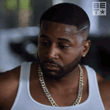 a man wearing a white tank top with a gold chain around his neck