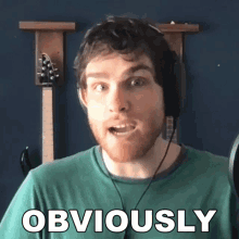 a man wearing headphones says obviously in front of a guitar rack