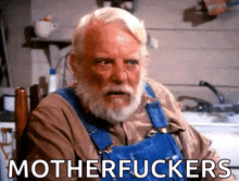 a man with a beard wearing blue overalls is sitting in a chair with the words motherfuckers below him