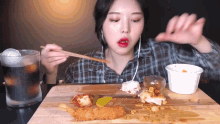 a woman in a plaid shirt is eating food with chopsticks on a wooden table