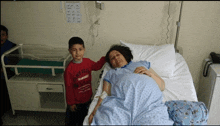 a boy standing next to a pregnant woman in a hospital bed wearing a shirt that says ' crew gear ' on it